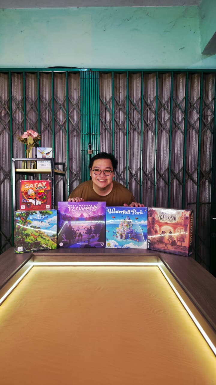Hendri tersenyum di belakang deretan kotak boardgame